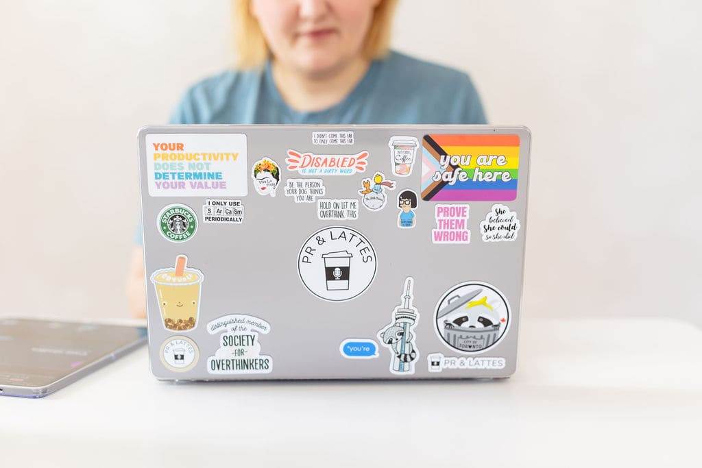 Matisse sits in front of her laptop, covered in various stickers about PR and Lattes, coffee, raccoons, being an over thinker, and providing a safe space.