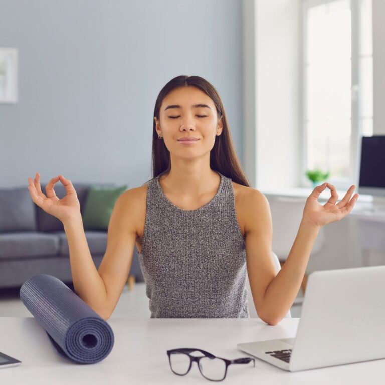 A woman meditates while sitting in front of her laptop.