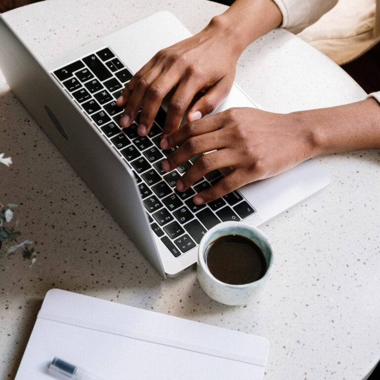 An overhead view of someone working away on their laptop with a cup of coffee next to it on the table.