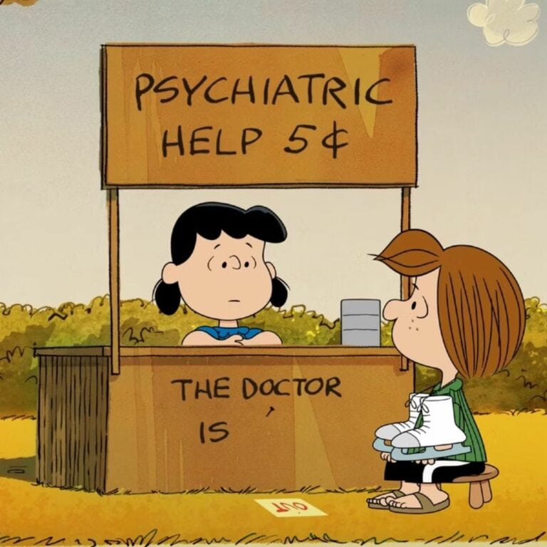 A still from a Charlie Brown episode with Lucy sitting at her psychiatric booth with Peppermint Patty seated in front of it waiting.
