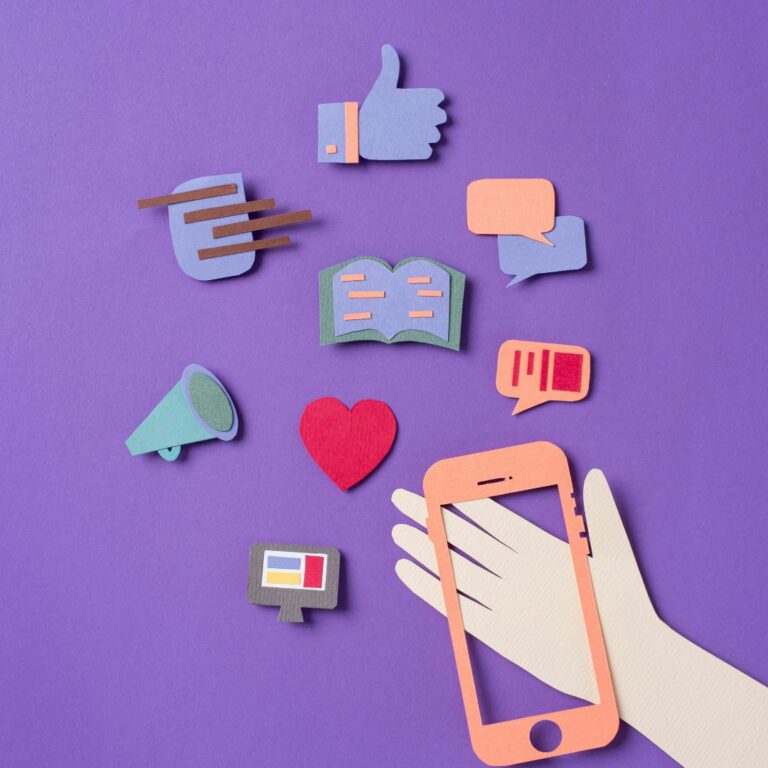 Construction papers cutouts of a hand holding a smartphone and various social media icons. The cutouts sit on a purple background.