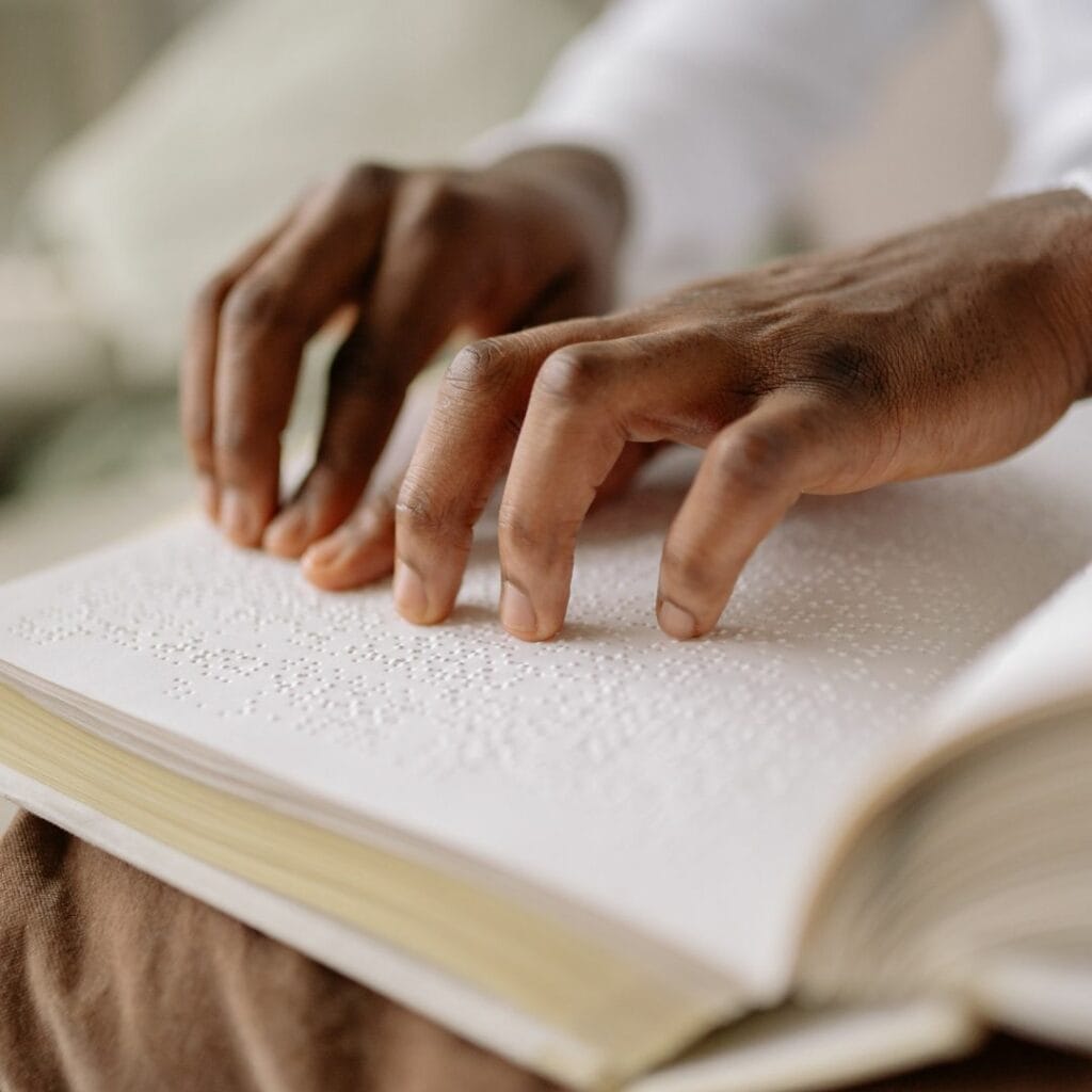 A close-up of a Black person's hands reading a braille book.