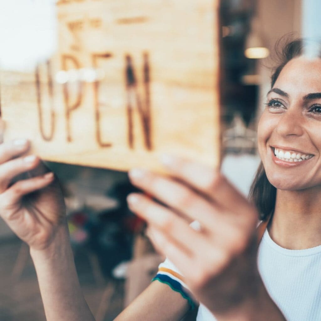 A woman smiles as she puts an open sign on the door of her business.