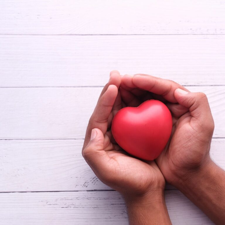 A close-up of a person holding a red heart in their hands.
